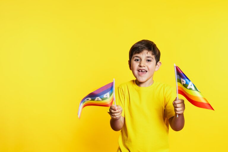 Joyful Boy Waving Peace Rainbow Flags on Yellow Background